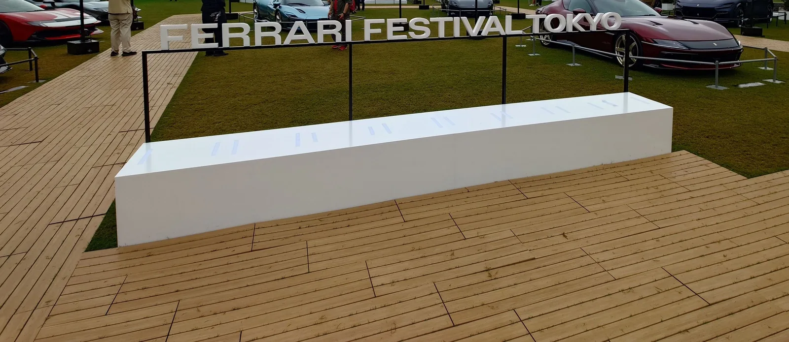 芝生の広場の入口に置かれた「FERRARI FESTIVAL TOKYO」の看板。奥に展示車が並んでいる